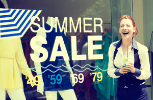 Young woman smiling in front summer sale decal on store window
